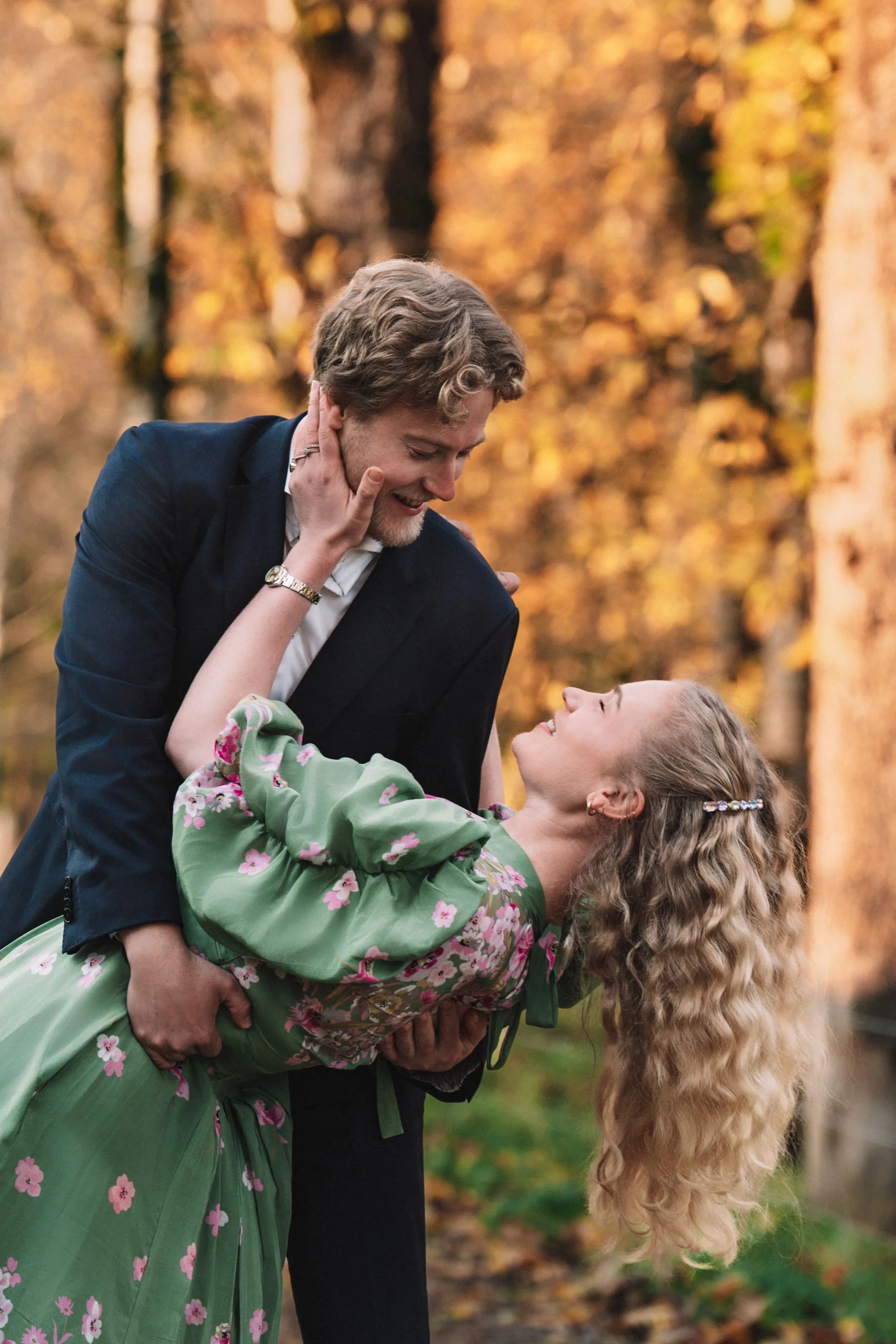 Han bøyer henne bakover blant høstløv, hun ser opp på ham